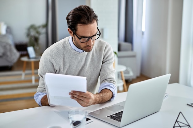 young businessman going through paperwork using laptop while working home 637285 5991 - Web Nômade Digital