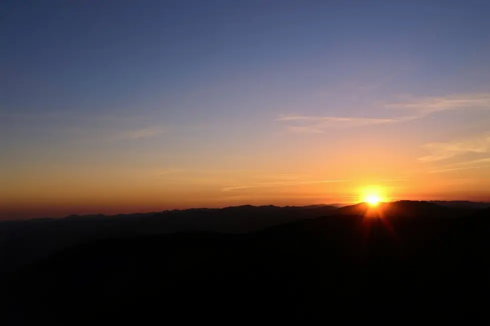 Pessoa contemplando o pôr do sol em uma montanha.