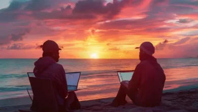 Um nômade digital utilizando um laptop na praia ao pôr do sol.