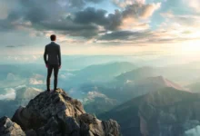 Empresário no topo de uma montanha olhando para oportunidades de crescimento.