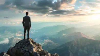 Empresário no topo de uma montanha olhando para oportunidades de crescimento.