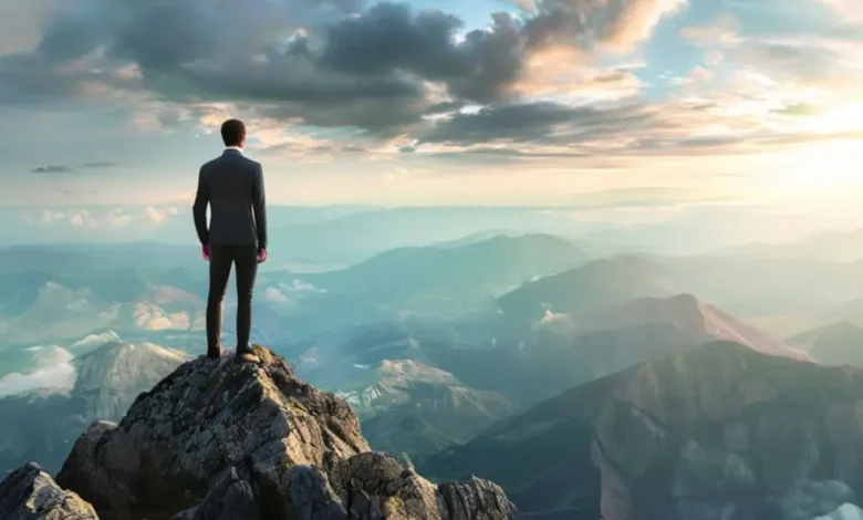 Empresário no topo de uma montanha olhando para oportunidades de crescimento.