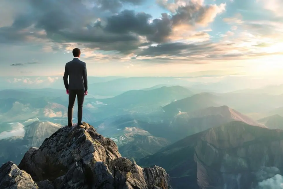 Empresário no topo de uma montanha olhando para oportunidades de crescimento.
