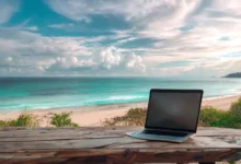 Laptop aberto em uma mesa de madeira, olhando para uma praia, simbolizando a liberdade do empreendedorismo digital.