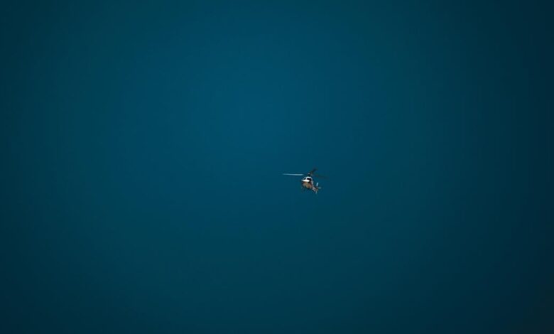 A small helicopter hovers alone in a vast, clear blue sky, symbolizing freedom and isolation.