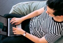 A man in a striped shirt using a laptop on a bean bag, embodying relaxed productivity.