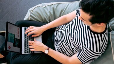 A man in a striped shirt using a laptop on a bean bag, embodying relaxed productivity.