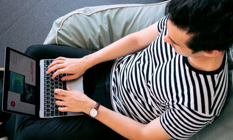 A man in a striped shirt using a laptop on a bean bag, embodying relaxed productivity.
