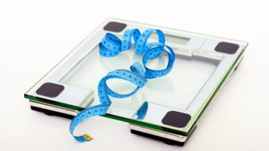 A digital glass weighing scale with a blue measuring tape, symbolizing weight management.