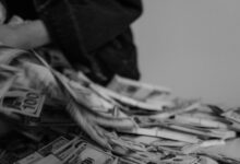 A blur of hands moving through a pile of US dollar bills, captured in black and white.