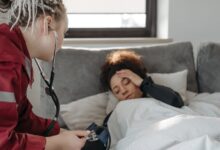 A paramedic examines a sick woman with a stethoscope indoors, providing medical care.