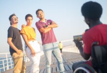 A joyful group of friends posing on a boardwalk, captured by a photographer in a wheelchair on a sunny day.