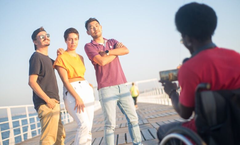 A joyful group of friends posing on a boardwalk, captured by a photographer in a wheelchair on a sunny day.