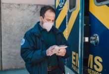 Paramedic in mask working next to EMS vehicle, preparing for emergency response.