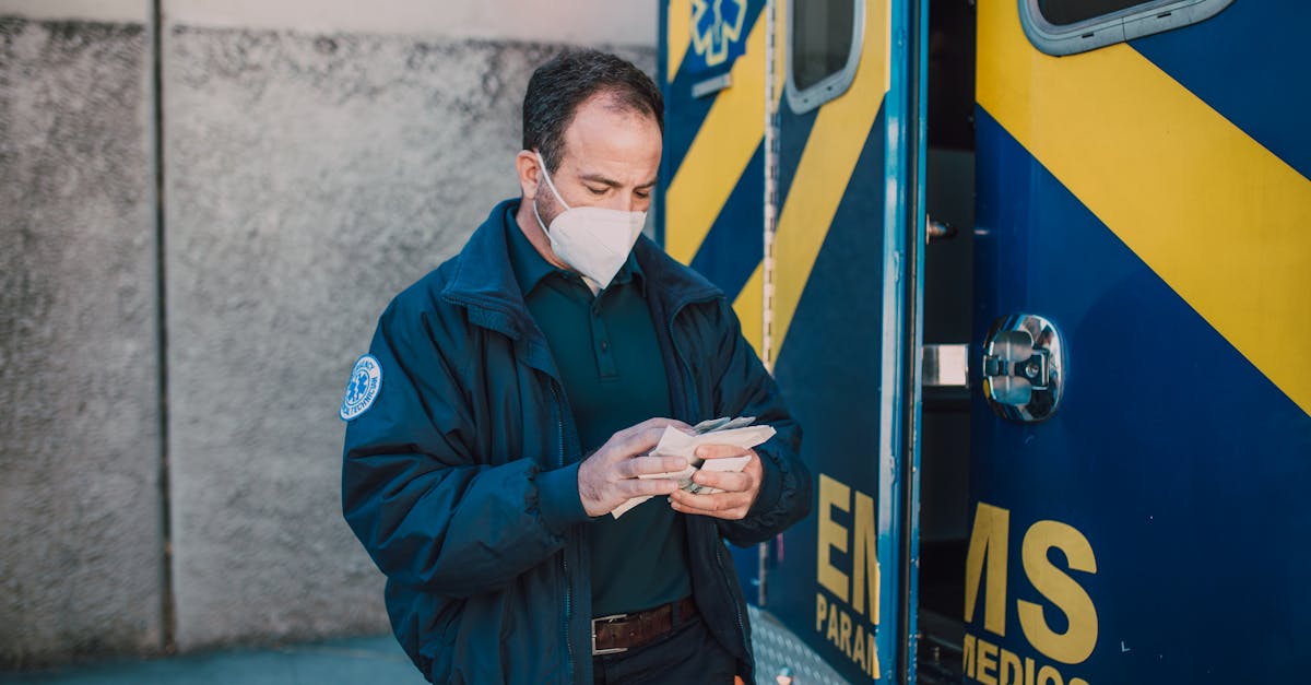 Paramedic in mask working next to EMS vehicle, preparing for emergency response.