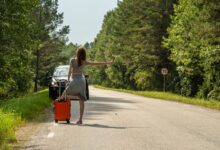 Woman hitchhiking with suitcase on roadside