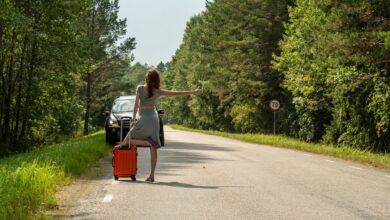 Woman hitchhiking with suitcase on roadside