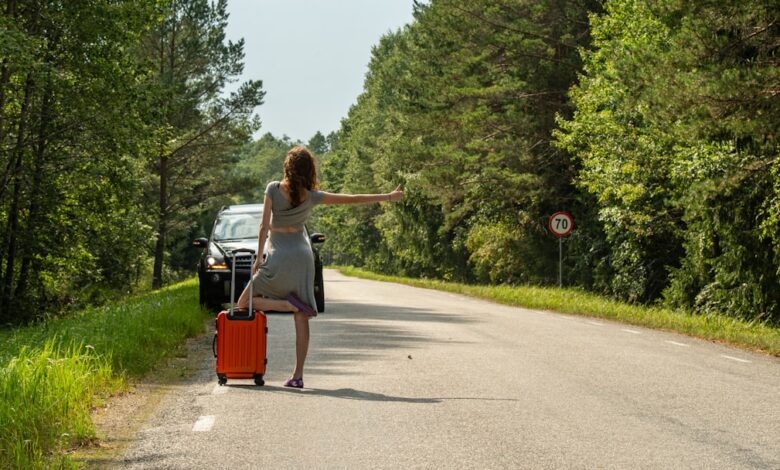 Woman hitchhiking with suitcase on roadside