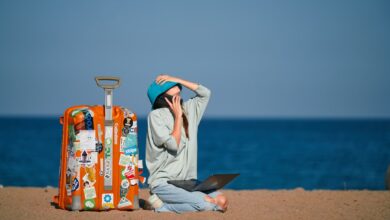 a person sitting on a beach with a suitcase and a laptop