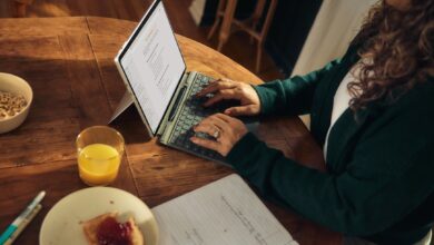 Woman typing on laptop at wooden table with breakfast.