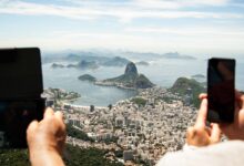 two person holding tablet computer and smartphone in elevated place with the view of city during daytime