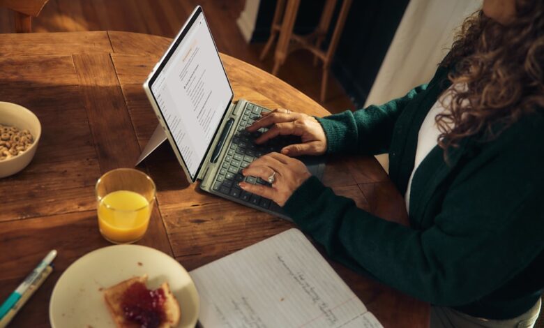 Woman typing on laptop at wooden table with breakfast.
