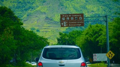 a silver car driving down a road next to a lush green hillside