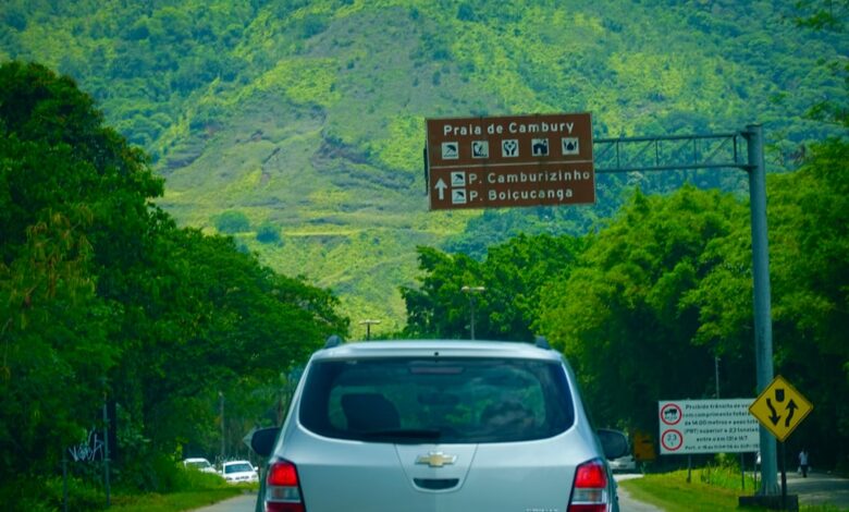 a silver car driving down a road next to a lush green hillside