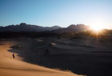 a person is walking in the desert at sunset