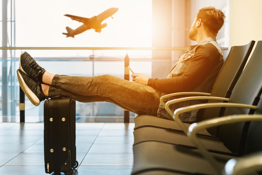 Como Aproveitar a Telemedicina Durante Viagens pelo Mundo - Web Nômade Digital man sitting on gang chair with feet on luggage looking at airplane