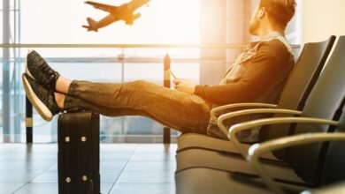 Como Economizar em Viagens: Dicas para Nômades Digitais - Web Nômade Digital man sitting on gang chair with feet on luggage looking at airplane