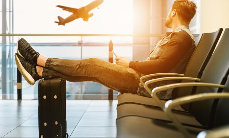 Como Economizar em Viagens: Dicas para Nômades Digitais - Web Nômade Digital man sitting on gang chair with feet on luggage looking at airplane