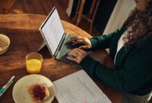 Woman typing on laptop at wooden table with breakfast