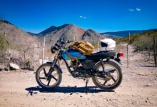 a motorcycle parked on a dirt road with mountains in the background