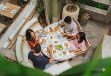 Four people dining at a tiled table with various small plates and drinks
