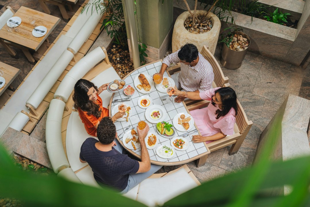 Four people dining at a tiled table with various small plates and drinks