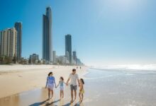 A family walking along the sandy beach in Surfers Paradise with city skyscrapers