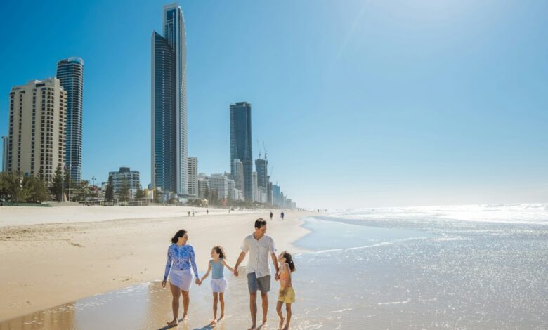 Como Encontrar o Equilíbrio entre Trabalho e Viagem como Nômade - Web Nômade Digital A family walking along the sandy beach in Surfers Paradise with city skyscrapers