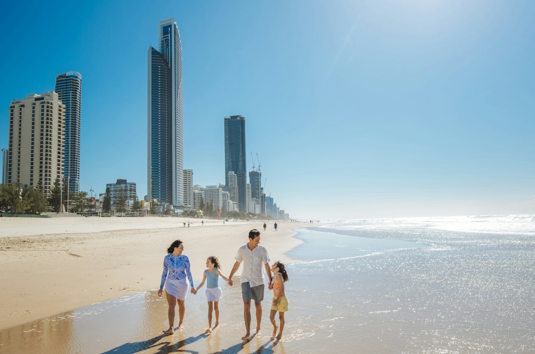 Como Encontrar o Equilíbrio entre Trabalho e Viagem como Nômade - Web Nômade Digital A family walking along the sandy beach in Surfers Paradise with city skyscrapers
