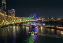 The Story Bridge illuminated at night above the Brisbane River with a ferry